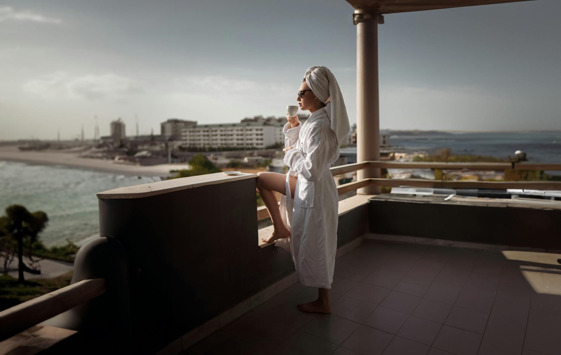 Kobieta w szlafroku pije drinka na balkonie z widokiem na morze