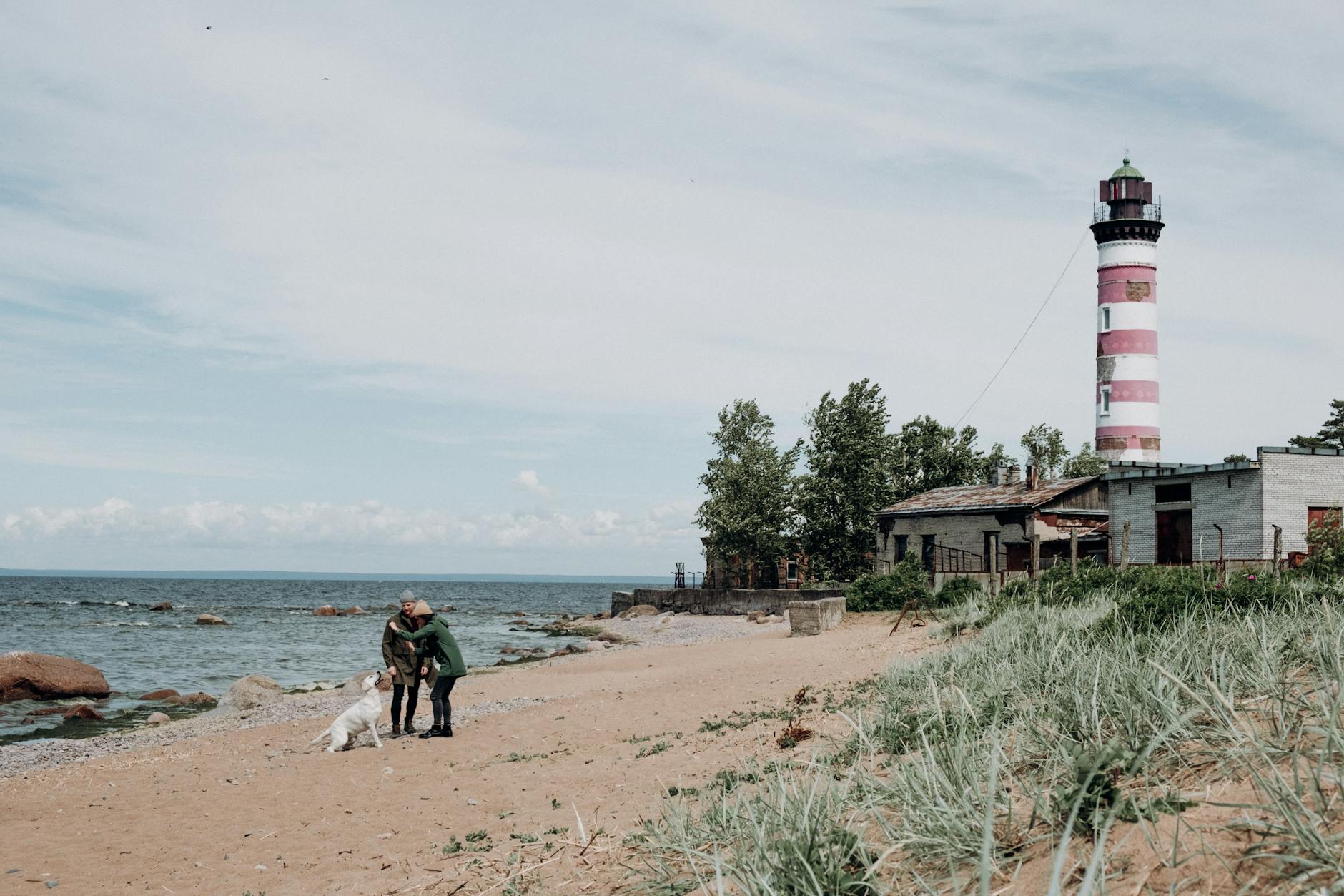 Rodzina z psem spaceruje przy latarni morskiej na bałtyckiej plaży