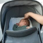 Śpiące niemowlę w wózku na spacerze, dotykane delikatnie przez dorosłego