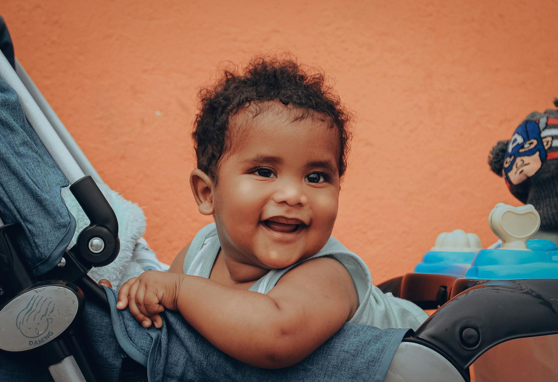 Uśmiechnięte niemowlę z kręconymi włosami siedzi wygodnie w wózku