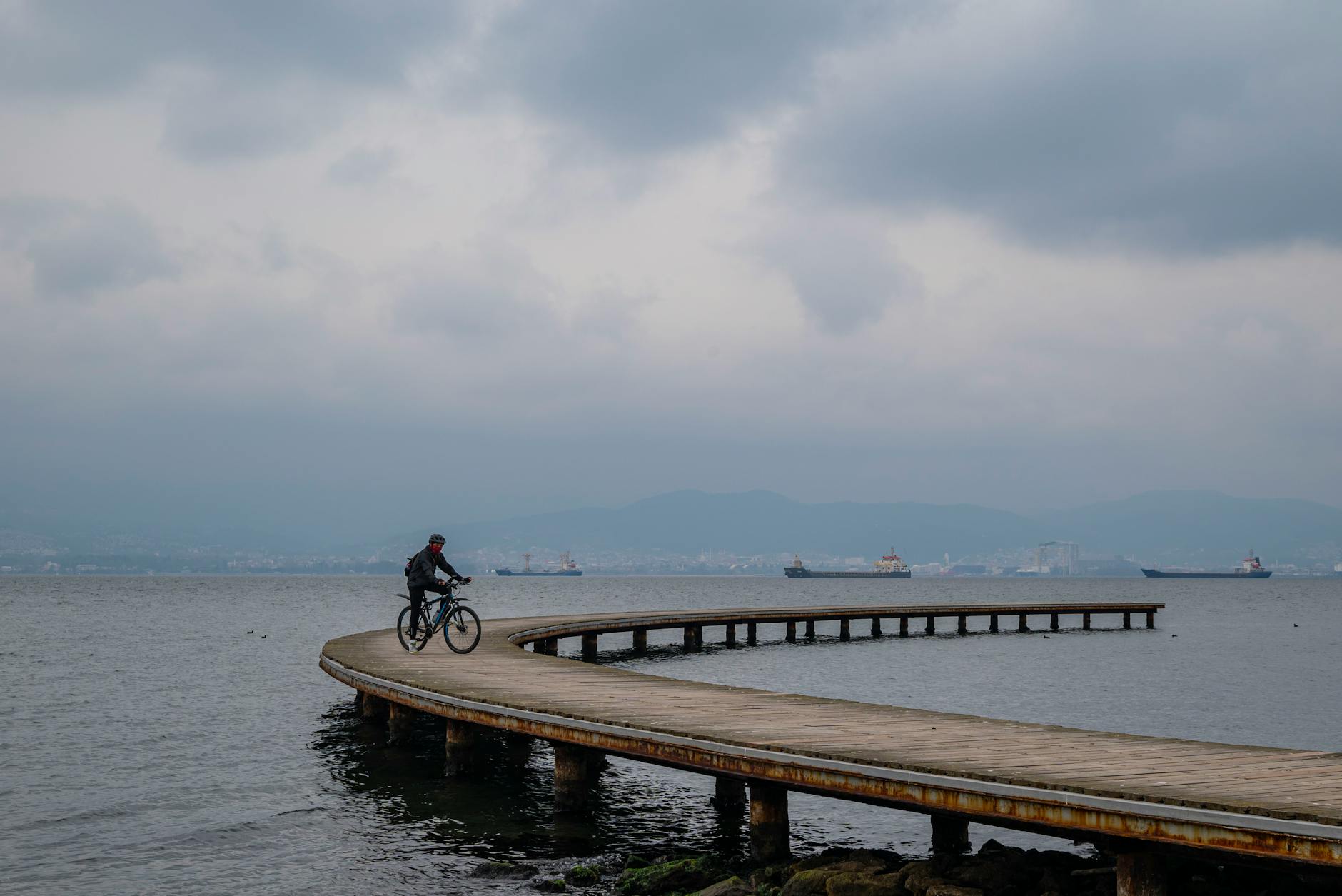 Rowerzysta jedzie po krętym molo nad spokojnym morzem pod zachmurzonym niebem