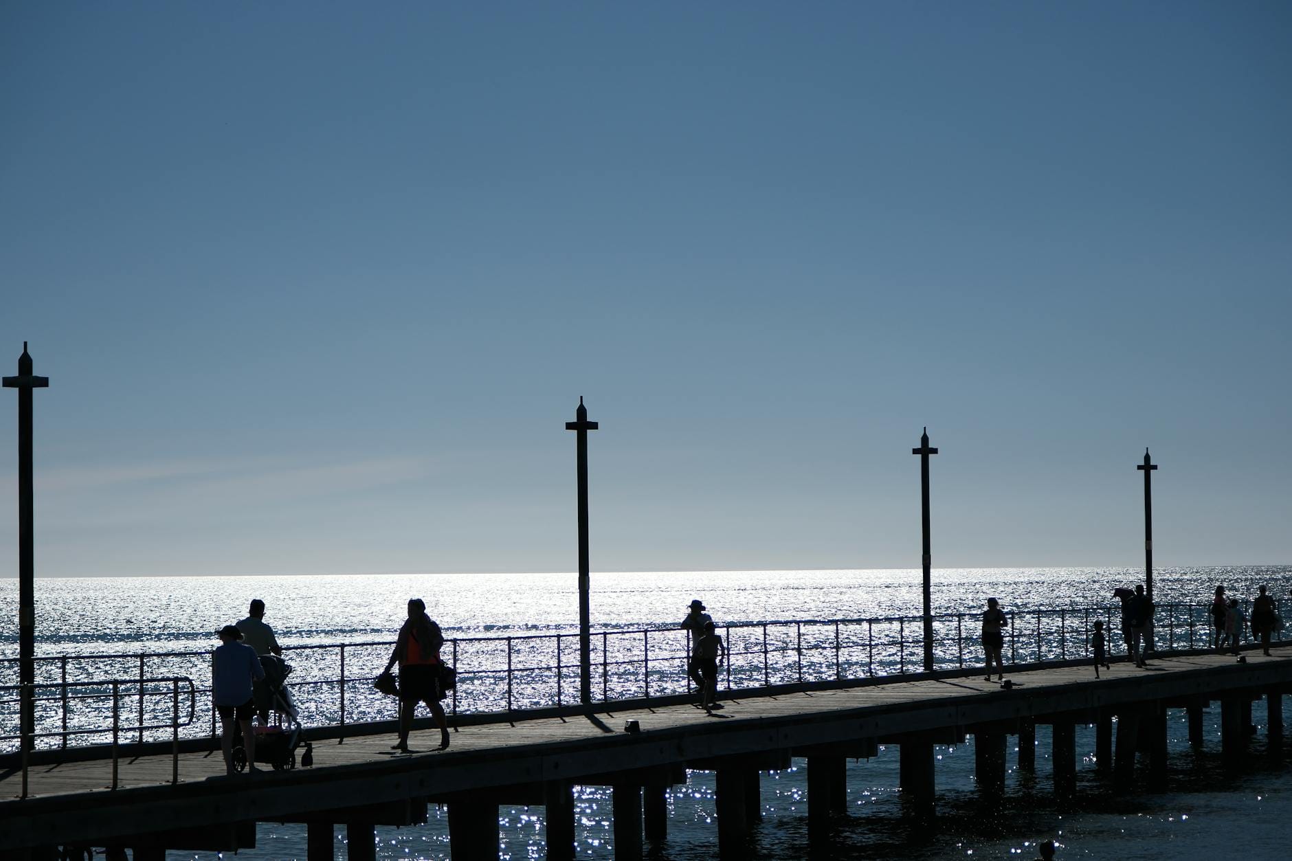 Sylwetki ludzi spacerujących po molo o zachodzie słońca nad morzem