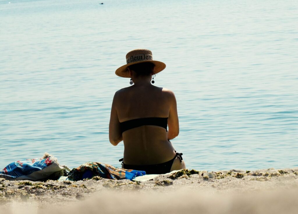 Kobieta w kapeluszu przeciwsłonecznym odpoczywa na plaży tyłem do aparatu