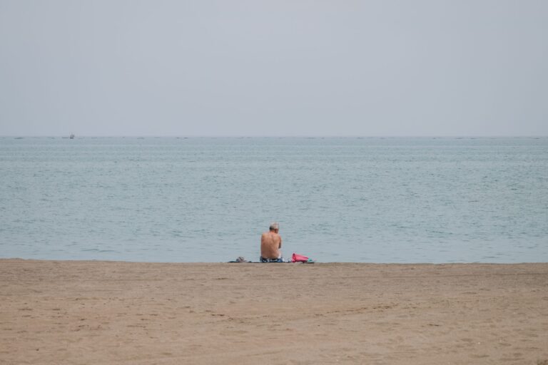 Starszy mężczyzna siedzący na piaszczystej plaży w Maladze